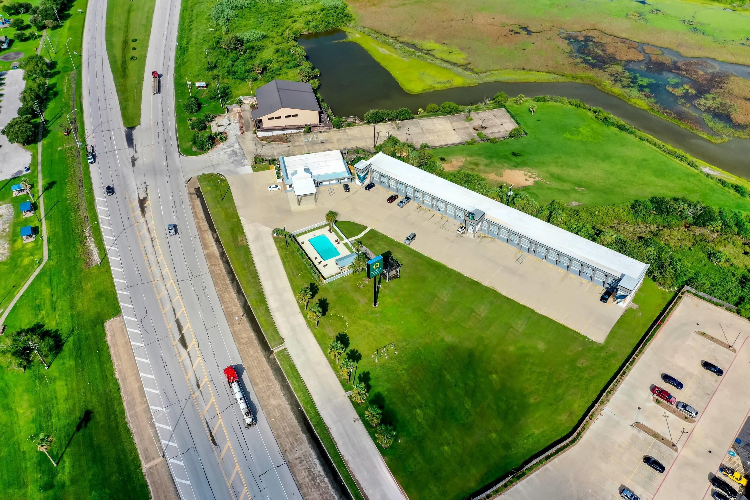 An aerial view of a building with a parking lot, a swimming pool, and a green field.