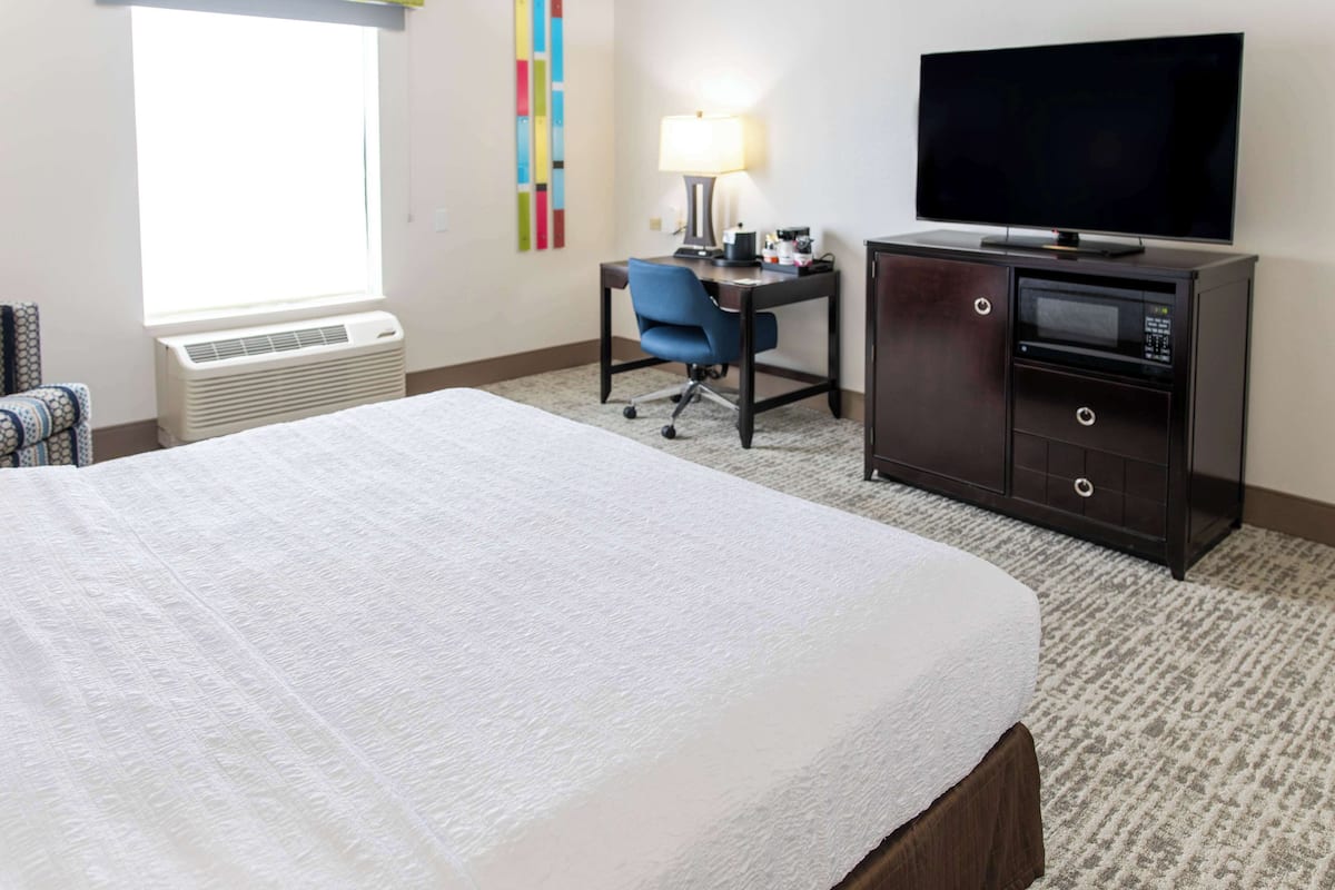 A hotel room with a bed, a desk with a chair, a television, and a minibar.