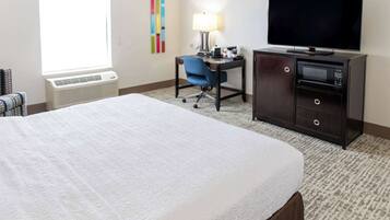 A hotel room with a bed, a desk with a chair, a television, and a minibar.