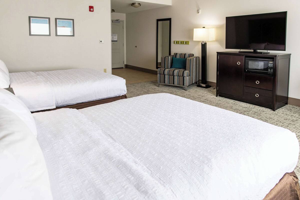 A hotel room with two beds, a TV, a microwave, a chair, and a lamp.