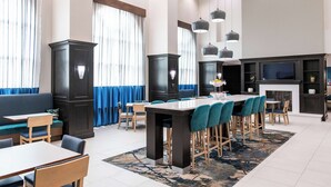 A modern hotel lobby with a long dining table, bar stools, a sofa, and a fireplace. - Hampton Inn & Suites Effingham (Effingham)