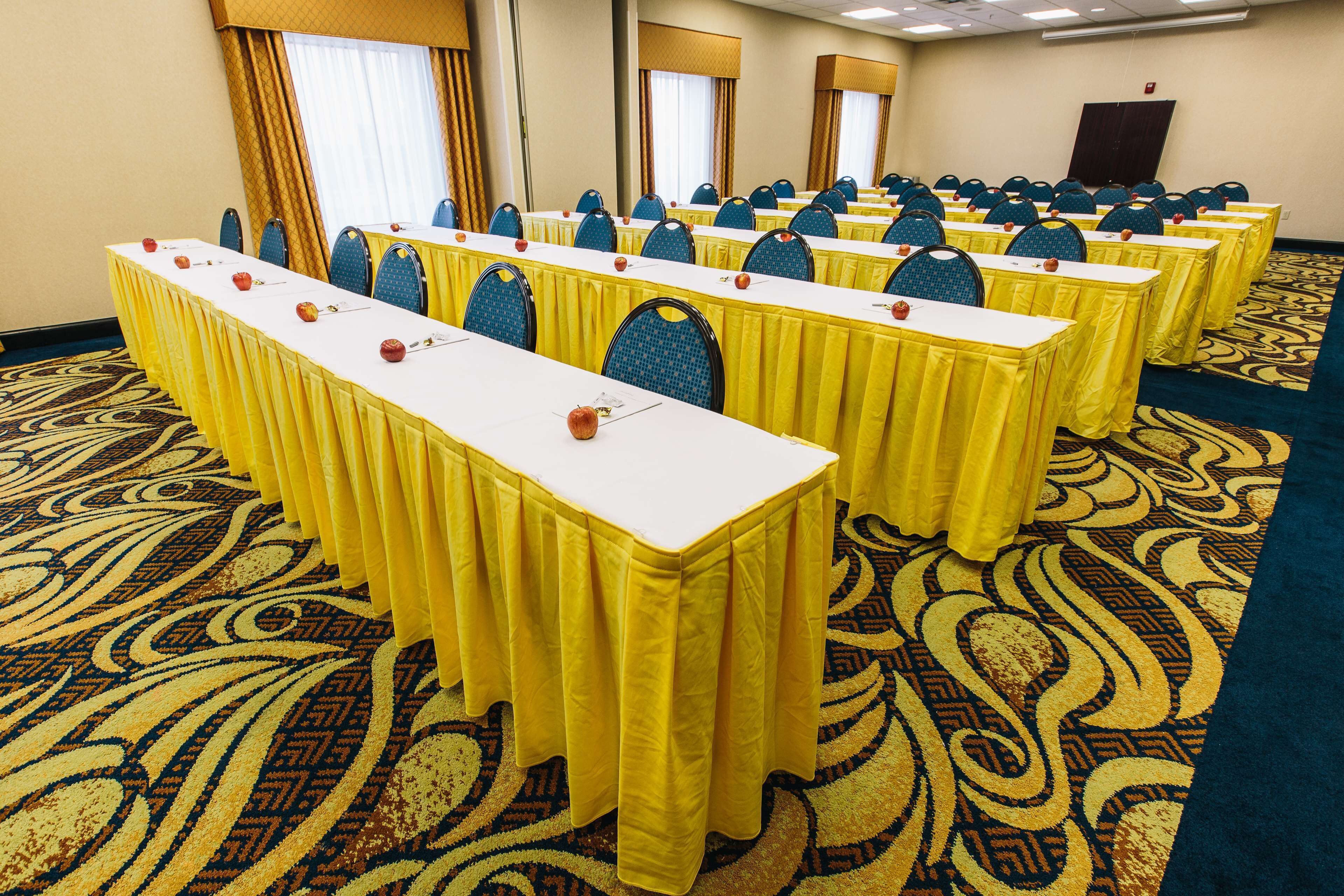 A conference room with multiple tables and chairs, carpeted floor, and large windows with curtains.