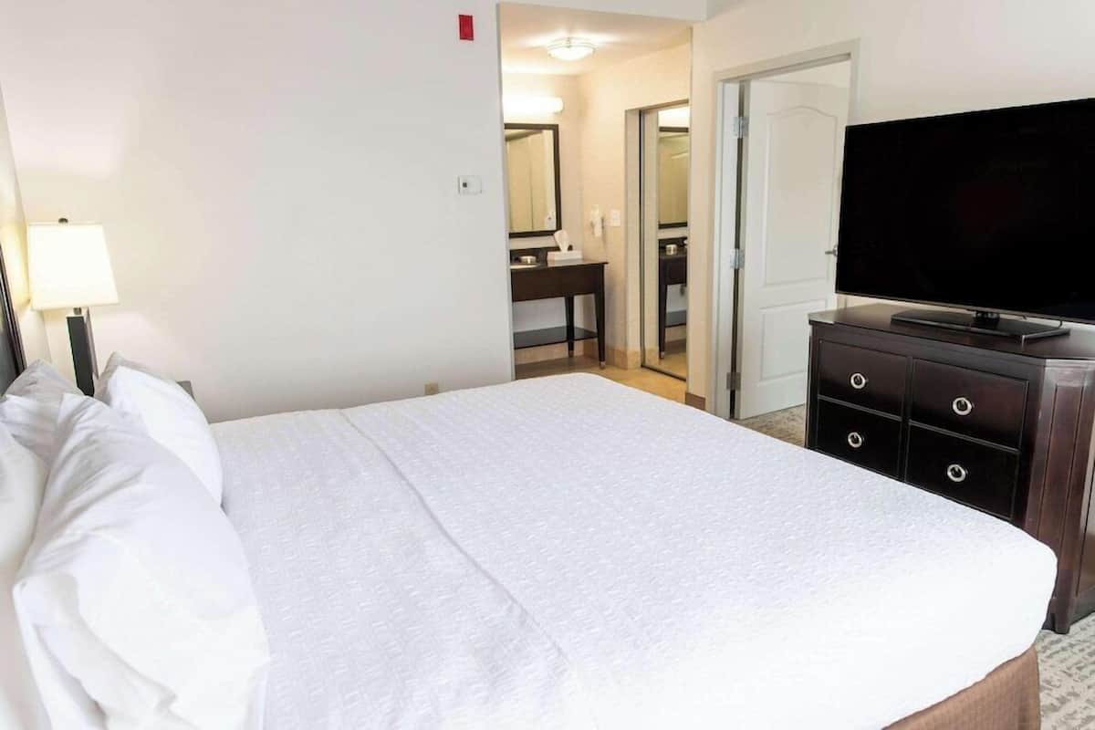 A hotel room with a large bed, a television on a dresser, and a bathroom visible through an open door.