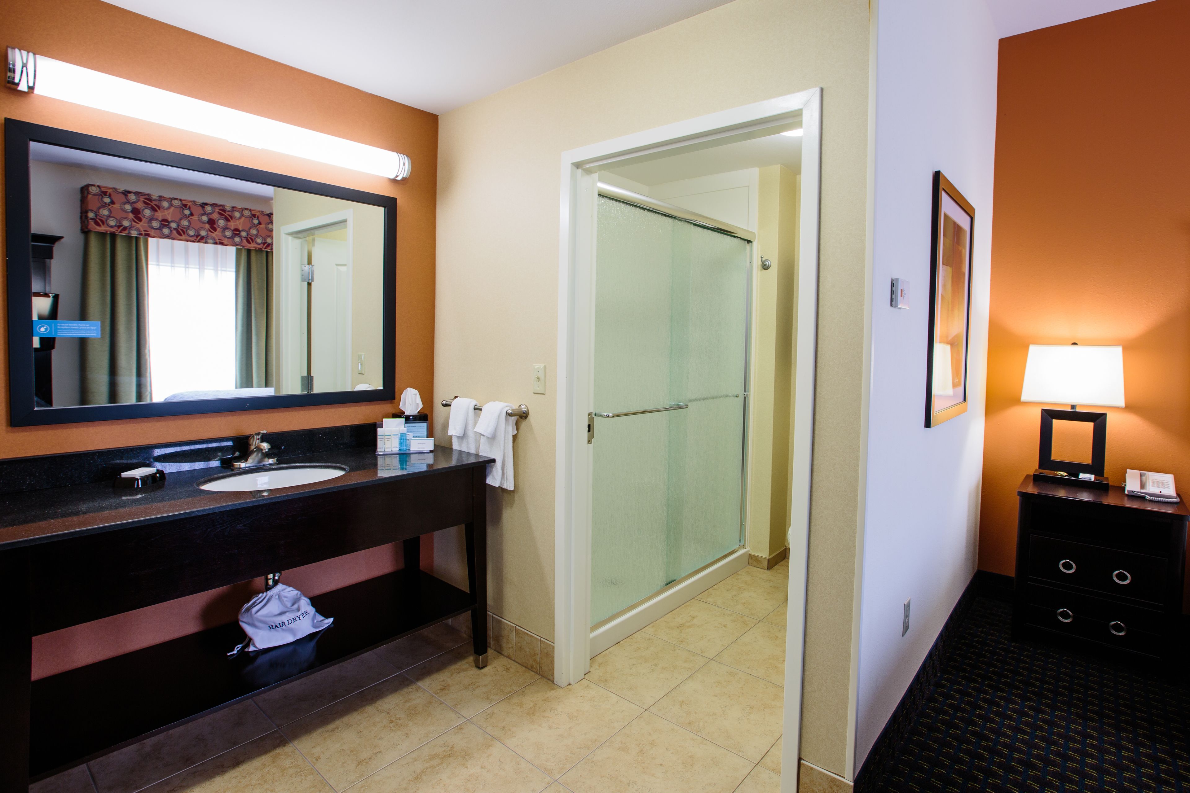 A hotel bathroom with a large mirror, a sink, a towel rack, and a shower.