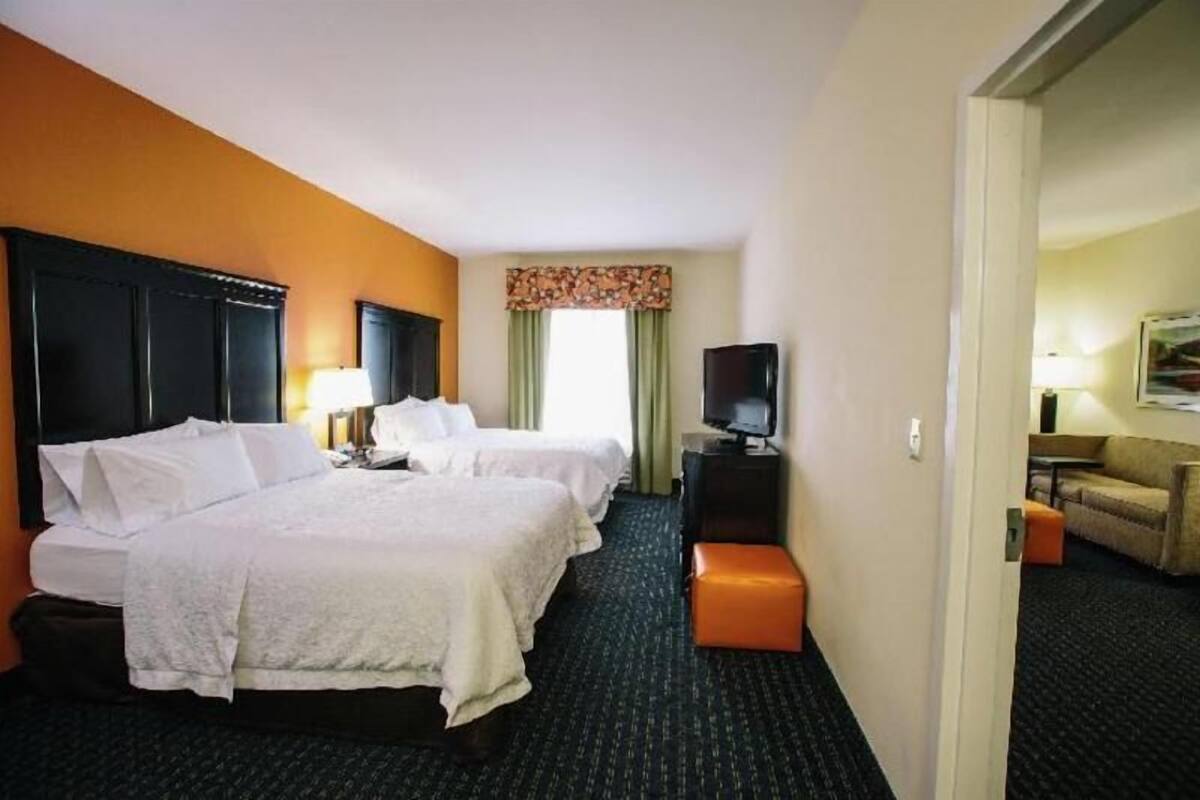 A hotel room with two beds, a television, a desk, and a small seating area.