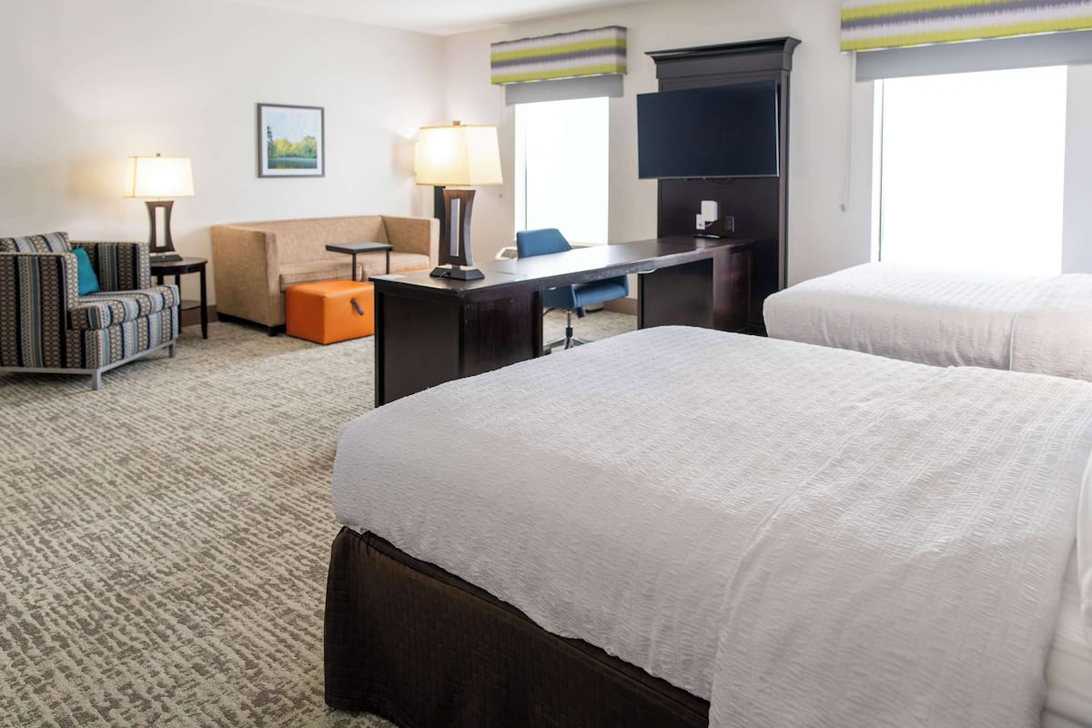 A hotel room with two beds, a desk, a chair, a sofa, and a TV.
