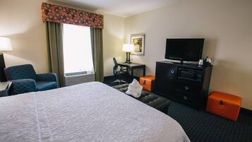 A hotel room with a large bed, a desk with a lamp, a television, a chair, and a dresser.