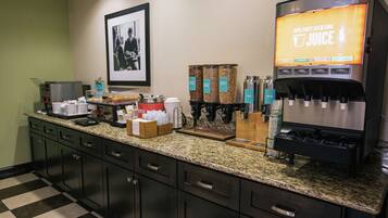 A hotel kitchen with a coffee station, a framed picture on the wall, and various food items on the counter.