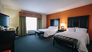 A hotel room with two beds, a desk with a TV, a chair, and a window with curtains.