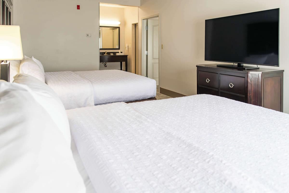 A hotel room with two beds, a television, a dresser, and a bathroom visible in the background.