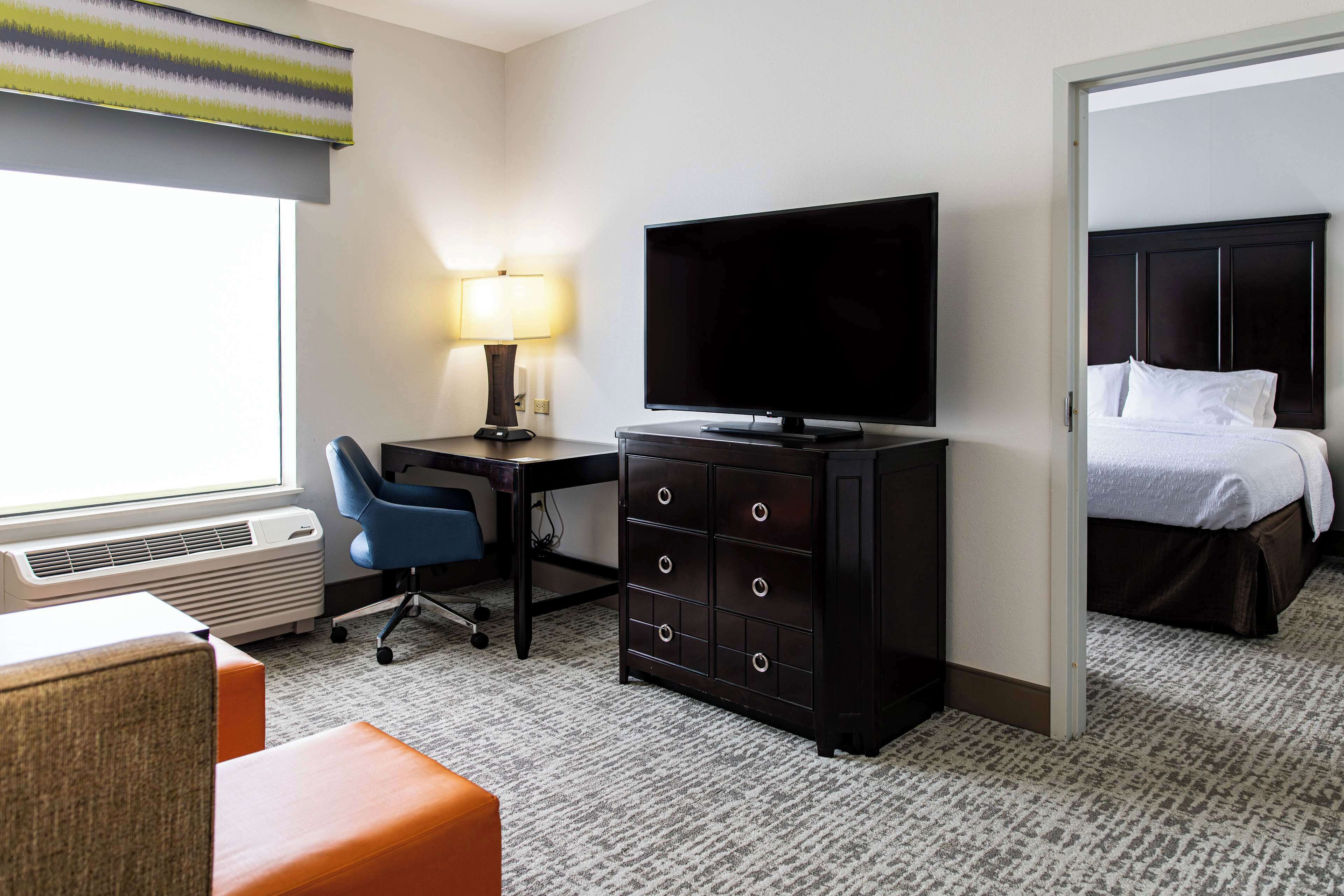 A hotel room with a desk, chair, television, dresser, and a bed.