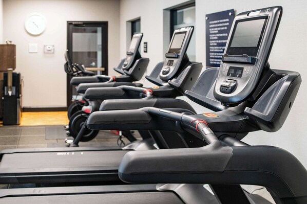 A row of stationary bikes with digital displays, a clock, and a sign with text on the wall.