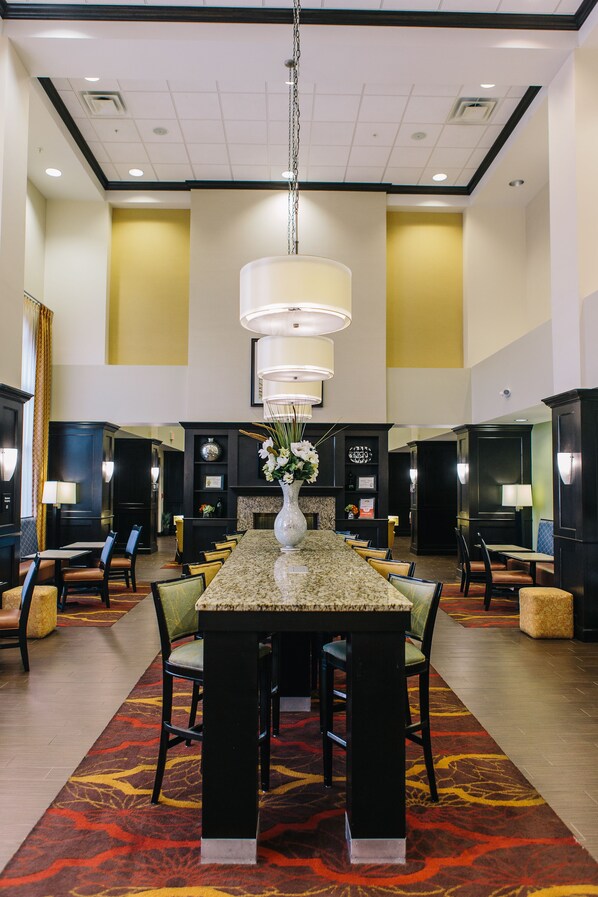 Un vestíbulo de hotel con una mesa central tipo isla, varias zonas de estar y un jarrón decorativo con flores.