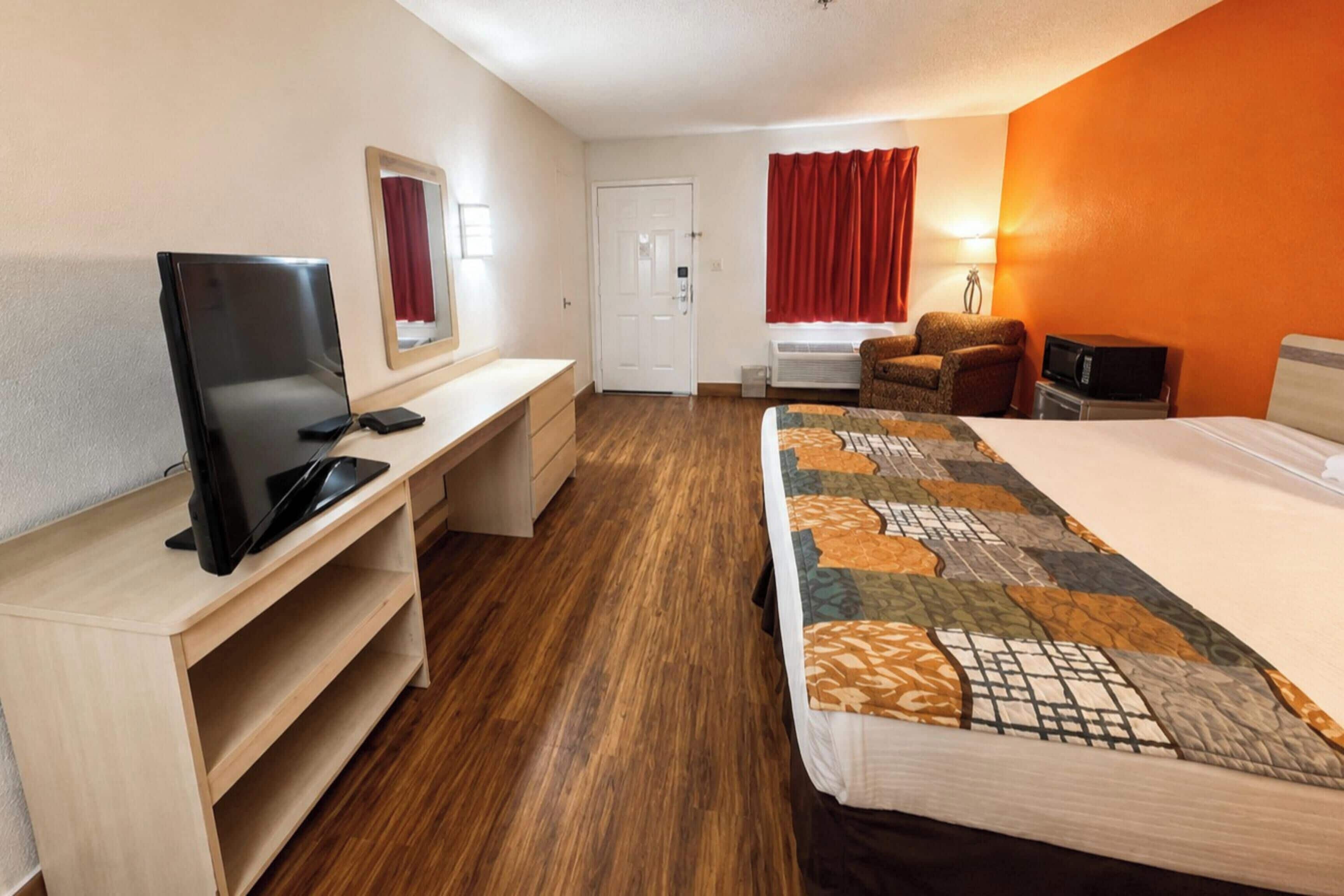A hotel room with a bed, a desk with a TV, a chair, and a window with curtains.