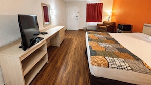 A hotel room with a bed, a desk with a TV, a chair, and a window with curtains. - Delta Inn West Helena US 49 AR (West Helena)