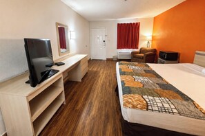 A hotel room with a bed, a desk with a TV, a chair, and a window with curtains.