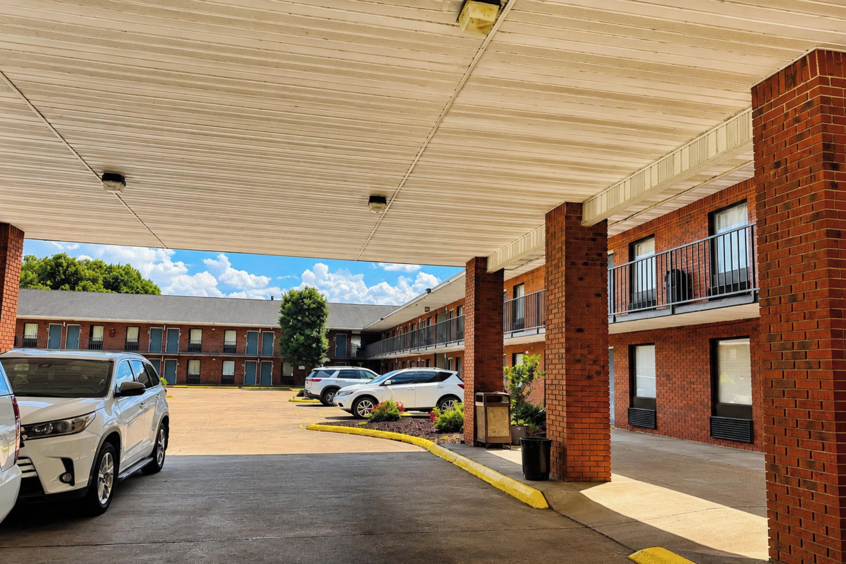 A parking lot with several cars, a covered walkway, and a building with brick walls and windows.