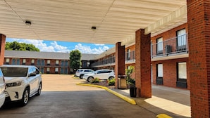 A parking lot with several cars, a covered walkway, and a building with brick walls and windows. - Delta Inn West Helena US 49 AR (West Helena)