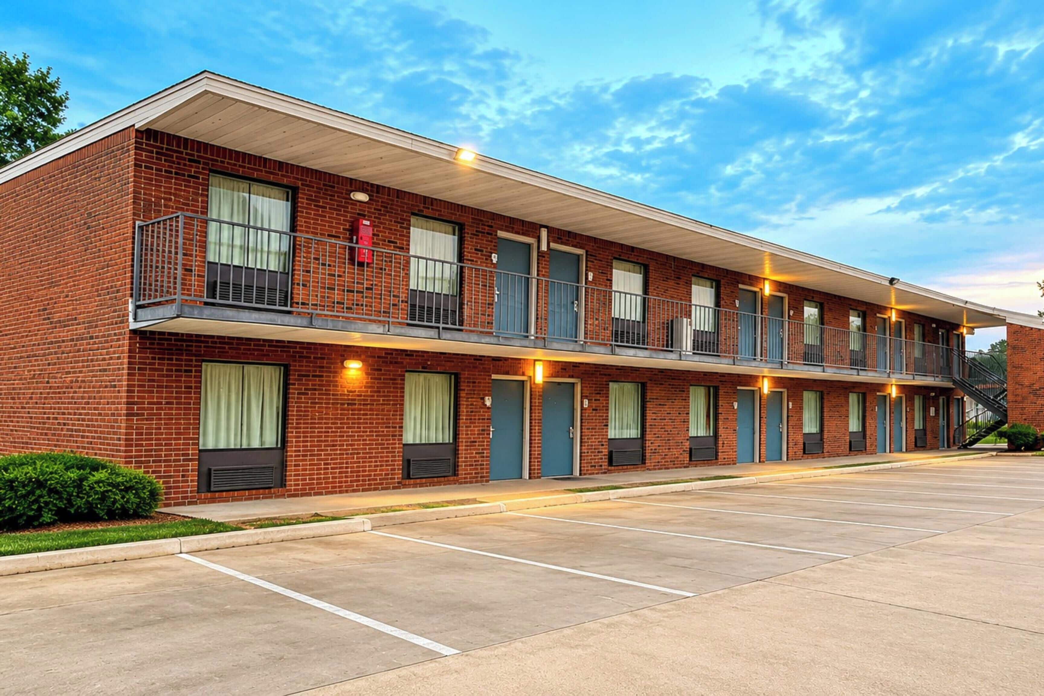 Un motel de varios pisos con fachada de ladrillo, balcones y estacionamiento.