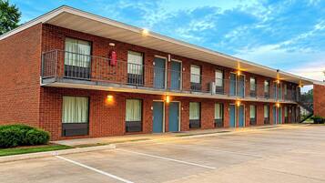 Un motel de varios pisos con fachada de ladrillo, balcones y estacionamiento.
