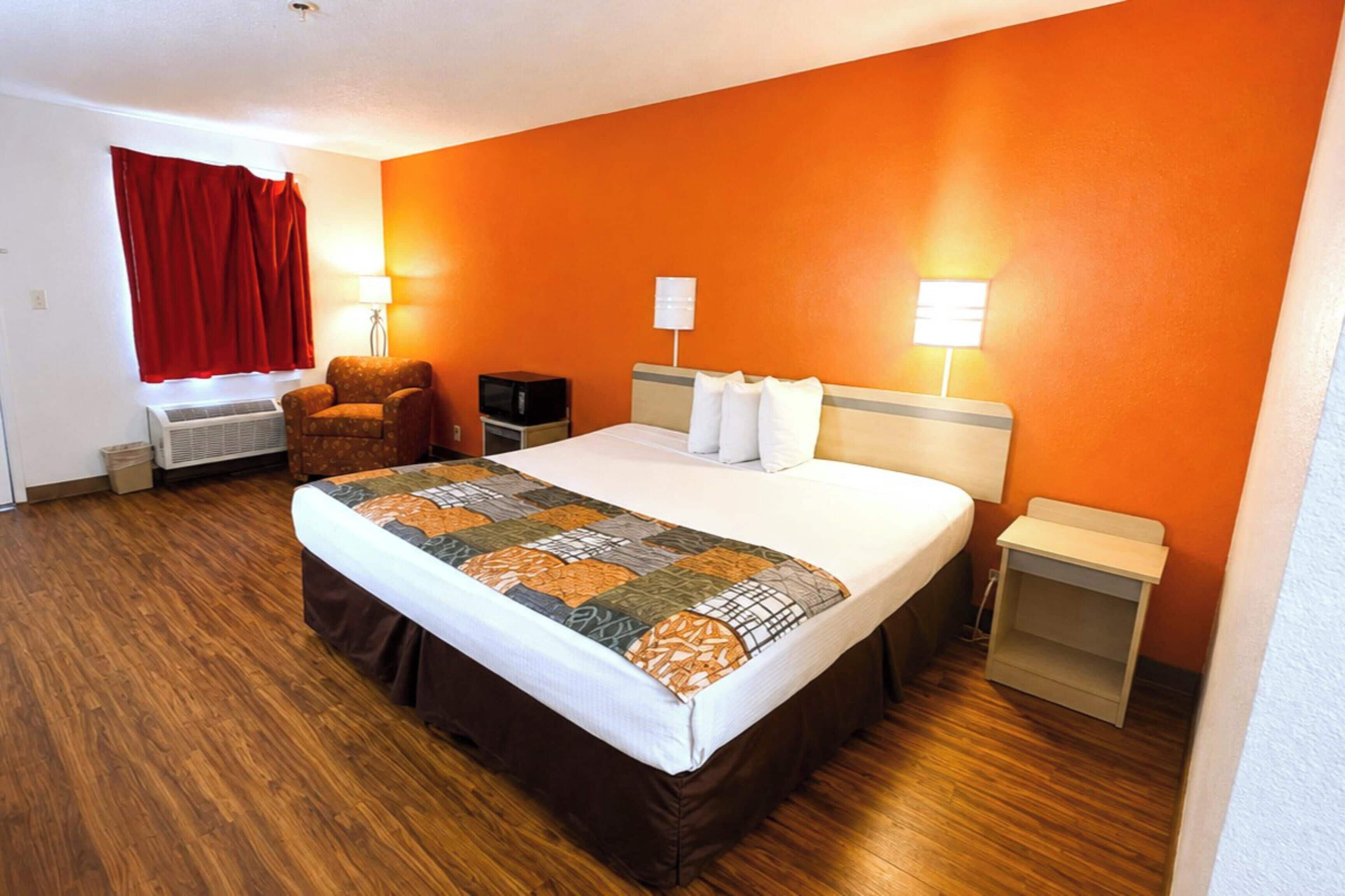 A hotel room with a large bed, two bedside tables, a chair, a TV, and a red curtain.