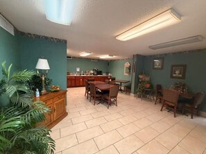 A dining area with a wooden table and chairs, a kitchen in the background, and green walls.