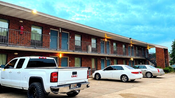 A multi-story motel with a brick facade, a covered parking area, and a staircase leading to the upper level. - Delta Inn West Helena US 49 AR (West Helena)