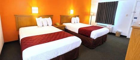 A hotel room with two beds, each with white linens and brown headboards, a bedside table with a telephone, and a window with curtains.