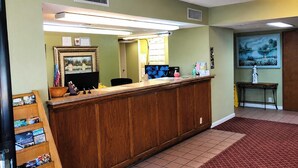 A reception desk with a wooden counter, a computer monitor, and various items on the desk. - Delta Inn West Helena US 49 AR (West Helena)