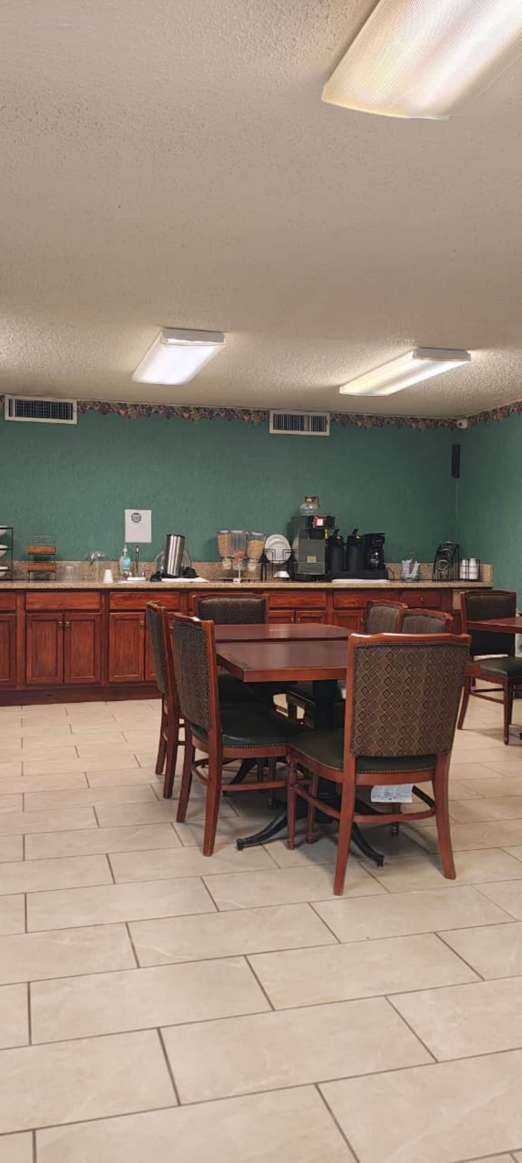 A dining area with a wooden table and chairs, a kitchen counter with appliances, and a green wall.