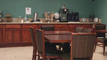 A dining area with a wooden table and chairs, a kitchen counter with appliances, and a green wall.