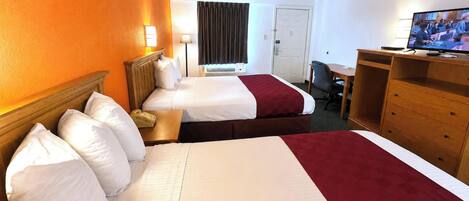 A hotel room with two beds, a desk, a television, and a door.