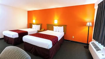 A hotel room with two beds, a desk, a chair, a lamp, and an air conditioning unit.