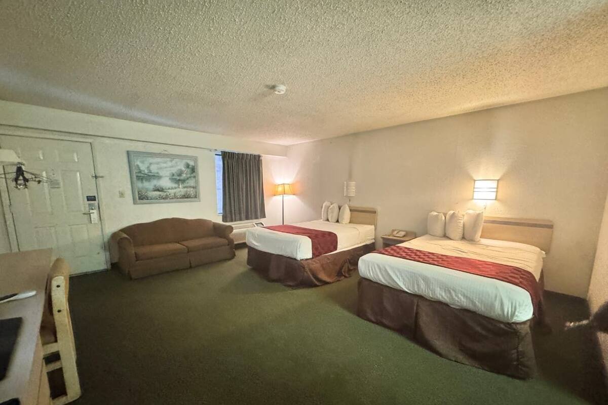 A hotel room with two beds, a sofa, a desk, and a door.
