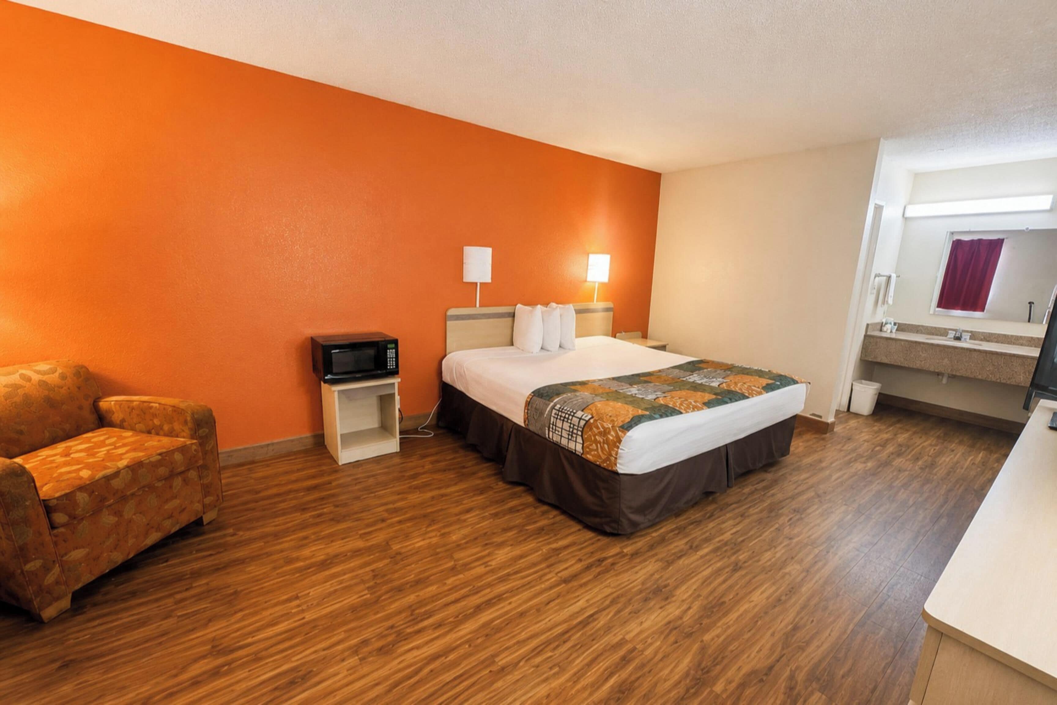 Una habitación de hotel con una cama, una silla, un escritorio, un televisor y un baño con espejo.