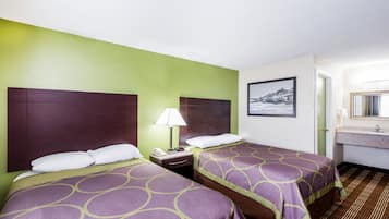 A hotel room with two beds, a nightstand with a lamp, a framed picture on the wall, and a bathroom with a sink and mirror.