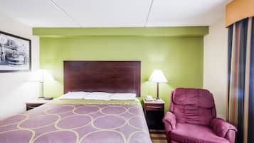 A hotel room with a large bed, two bedside tables with lamps, a wooden headboard, and a single purple armchair.