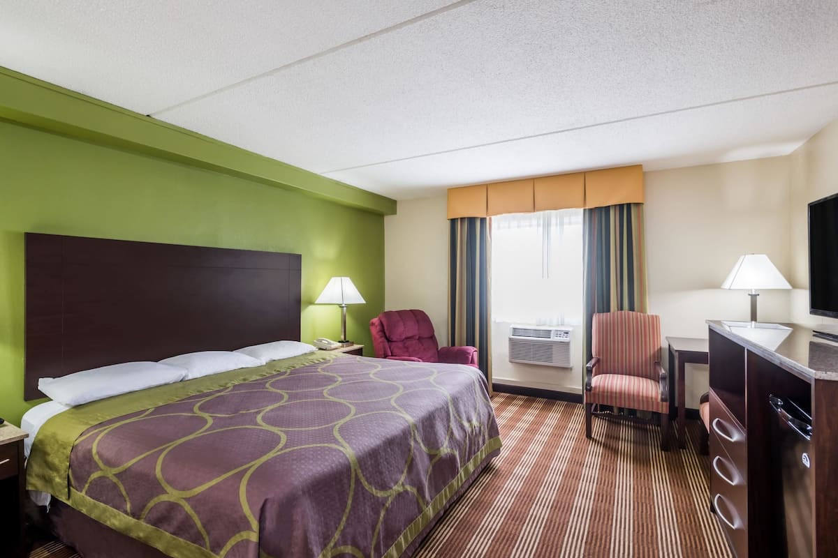Ein Hotelzimmer mit Bett, zwei Stühlen, Schreibtisch, Fernseher und Klimaanlage.