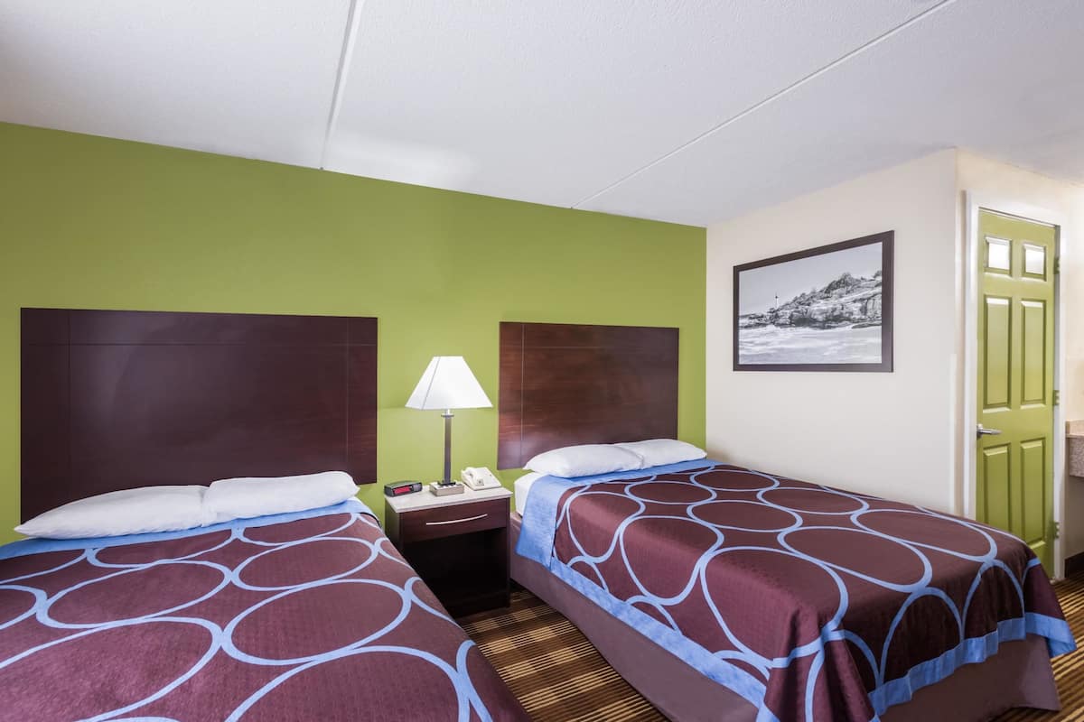 Ein Hotelzimmer mit zwei Betten, einem Nachttisch, einer Lampe und einem gerahmten Bild an der Wand.