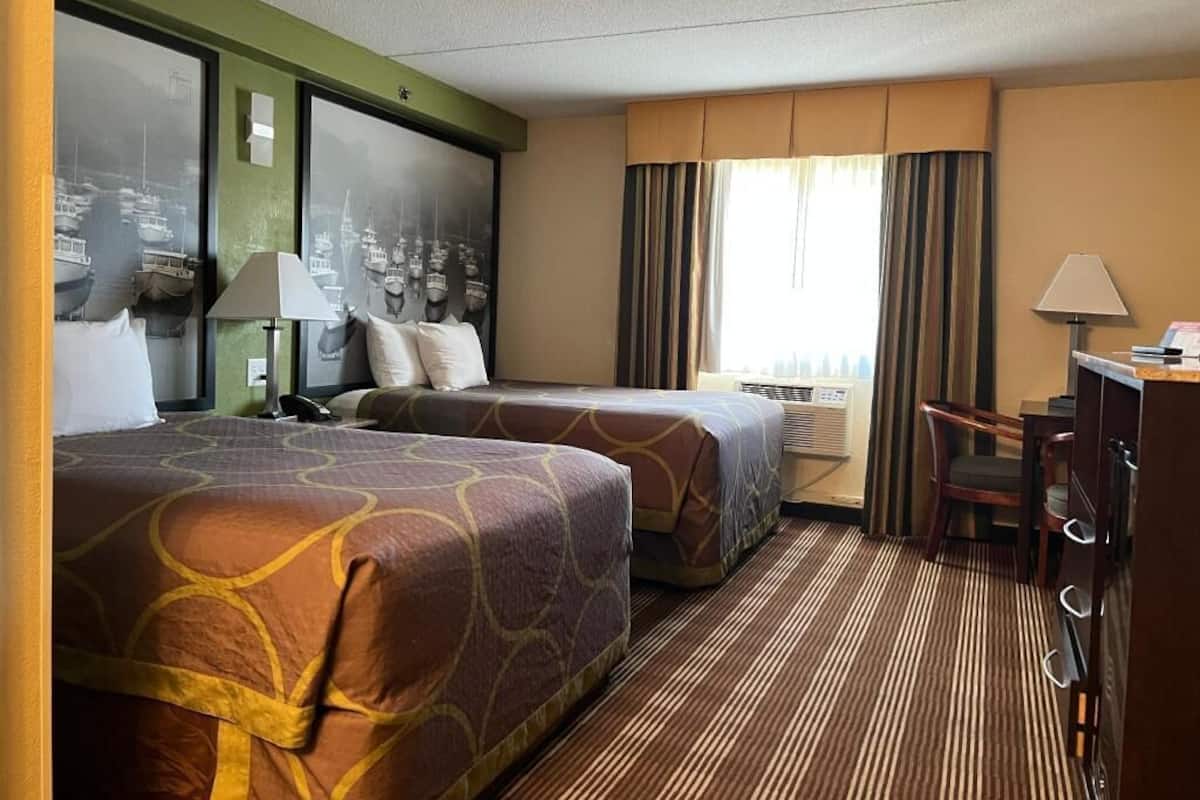 Ein Hotelzimmer mit zwei Betten, einem Schreibtisch, einem Stuhl, einer Lampe und einem großen Fenster mit Vorhängen.