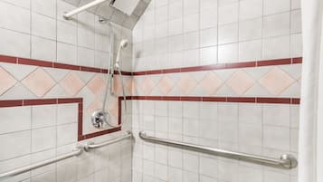 Zona de ducha con azulejos blancos, detalles en rojo y un cabezal de ducha de mano.