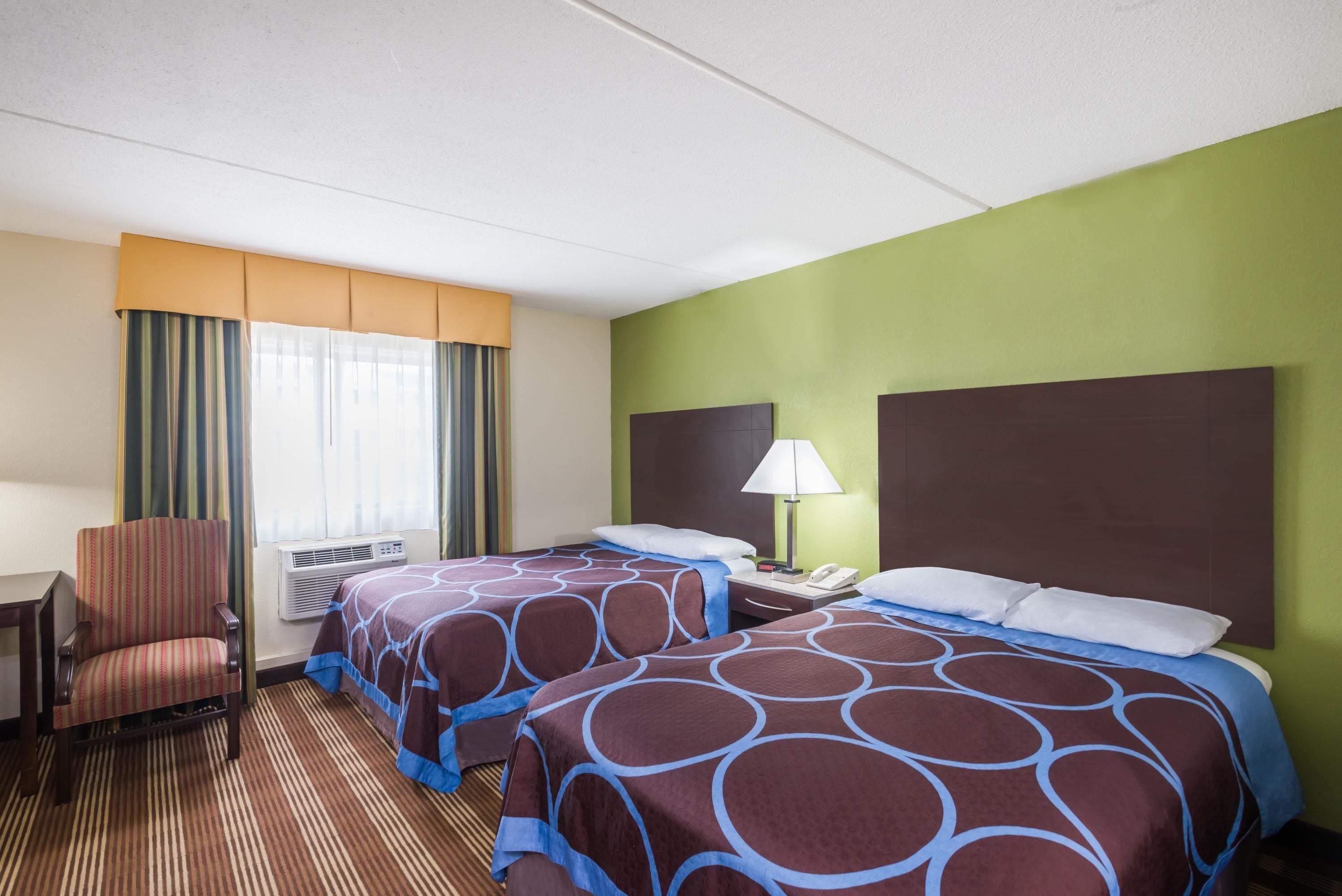 A hotel room with two beds, a chair, a desk, and a window with curtains.