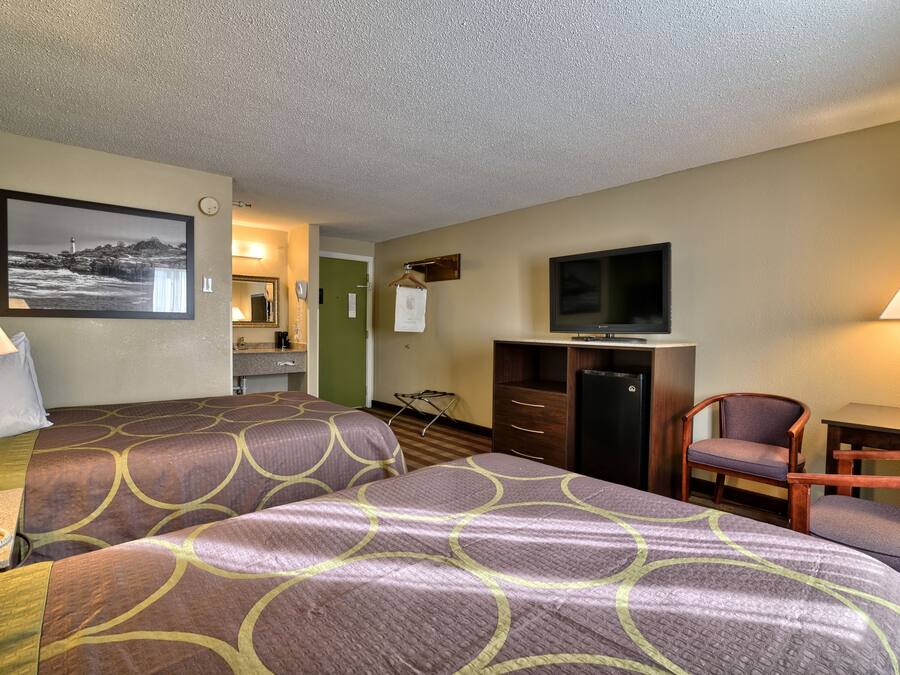 A hotel room with two beds, a television, a desk, a chair, and a painting on the wall.