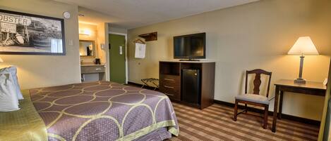 A hotel room with a large bed, a television, a desk with a lamp, a chair, and a dresser.