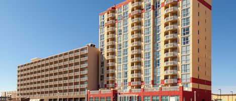 A multi-story hotel with a red and beige facade, multiple balconies, and a beachside location.