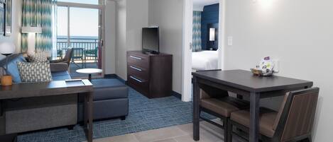 Habitación de hotel con balcón, sofá, televisión, escritorio y zona de comedor.