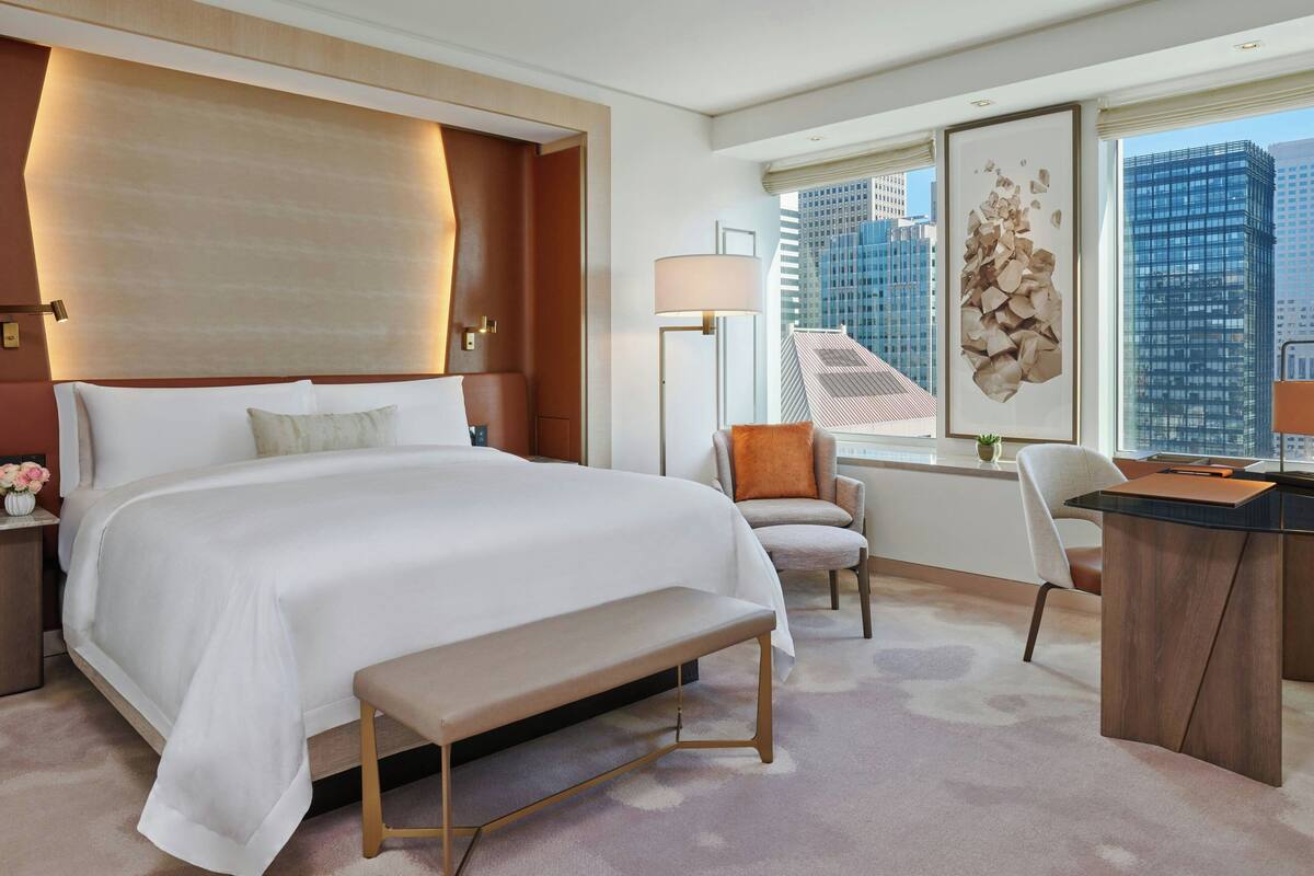 A modern hotel room with a large bed, a desk, and a view of city buildings.