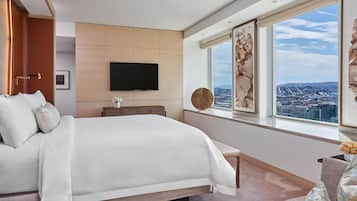 Een moderne slaapkamer met een groot bed, een flatscreen televisie aan de muur, een raam met uitzicht op de stad en een decoratief wandobject.
