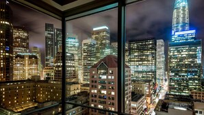 Un paisaje urbano nocturno visto a través de una ventana, con rascacielos iluminados y vistas de la ciudad.