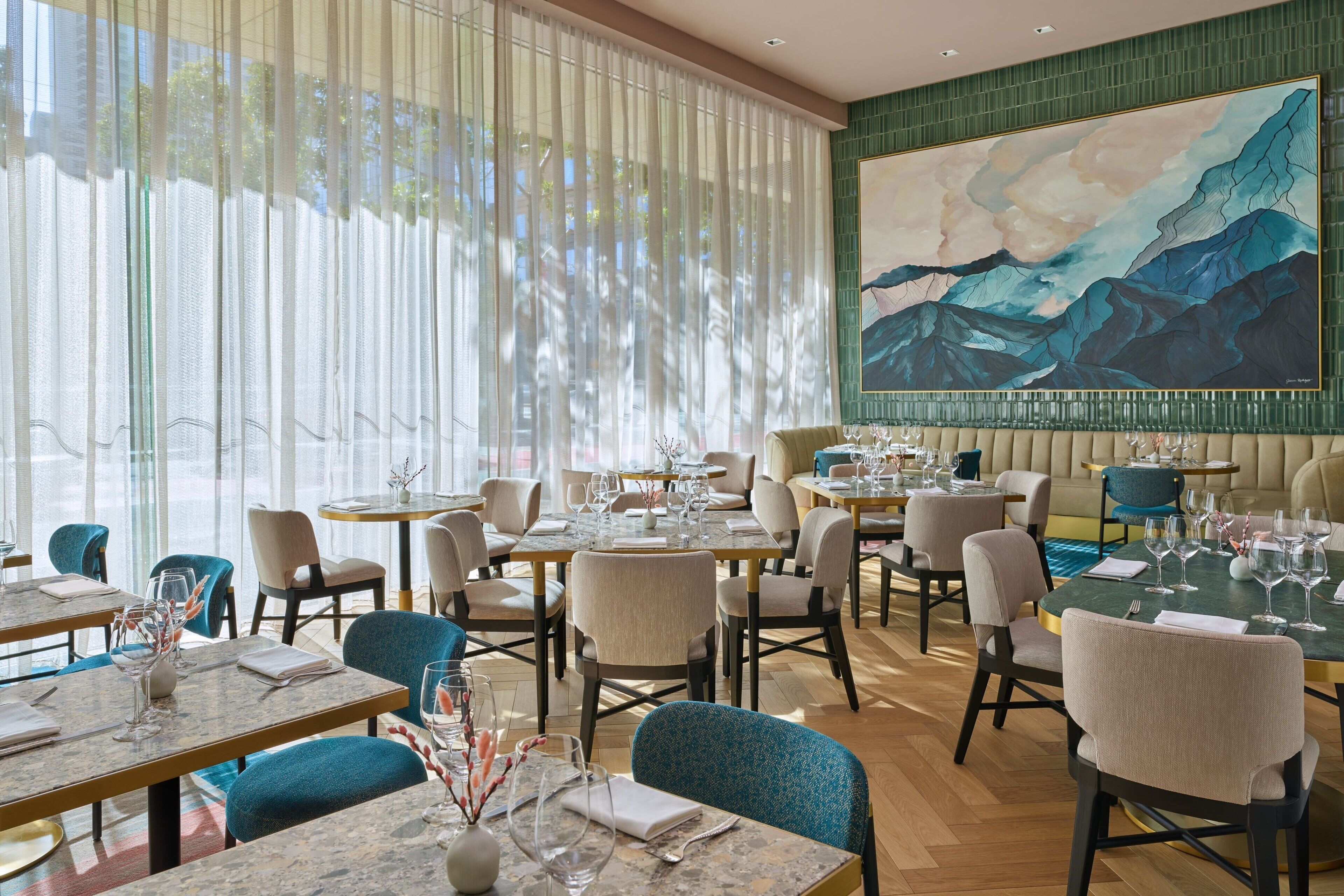 Un restaurant amb diverses taules i caires, i un quadre gran a la paret.